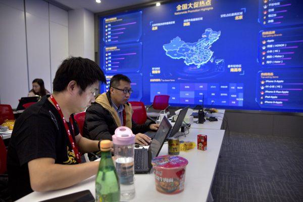 Workers use their laptops near a display showing sales data at the command center at the headquarters of an e-commerce retailer in Beijing on Nov. 11, 2018. (Mark Schiefelbein/AP)
