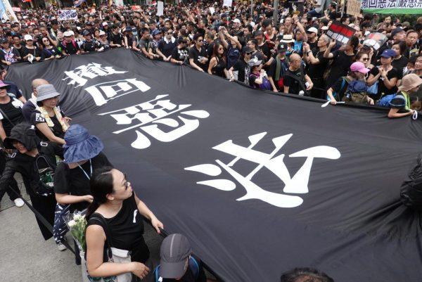 Protesters hold a large banner with the Chinese characters “Retract the Evil Law” in Wan Chai, Hong Kong, on June 16, 2019. (Yu Gang/The Epoch Times)
