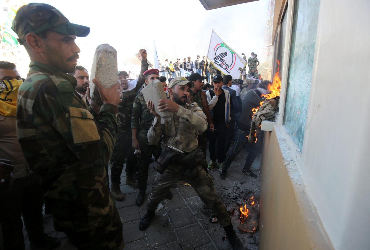 Members of the Hashed al-Shaabi, a terrorist group trained and armed by Iran, smash the bullet-proof glass of the U.S. embassy's windows in Baghdad with blocks of cement after breaching the outer wall of the diplomatic mission on Dec. 31, 2019. (Ahmad Al-Rubaye/AFP via Getty Images)