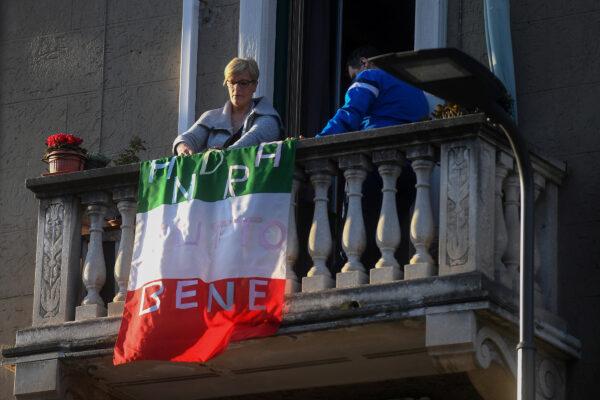 A woman places an Italian flag that reads "everything will be alright" on her apartment balcony as part of a flashmob organized to raise morale during Italy's coronavirus crisis, in Milan, Italy, on March 16, 2020. (Daniele Mascolo/Reuters)