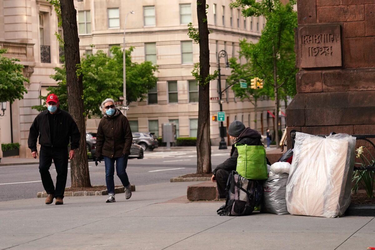 A man and woman wearing protective masks walk by a homeless person in New York City on May 4, 2020. (Cindy Ord/Getty Images)