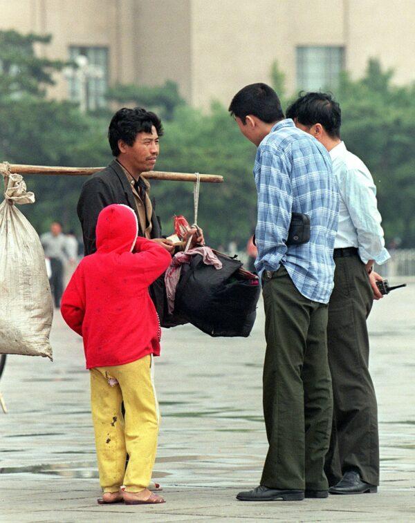 A 1998 file image of Chinese plain-clothes police questioning a peasant together with his child as they try to hawk their produce in Tiananmen Square in Beijing. (Goh Chai Hin/AFP via Getty Images)