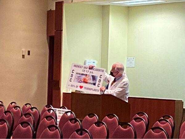 A Loudoun County physician James Norconk Jr. shows a sign stating the heart inflammation side effect of the COVID-19 vaccines on age group 12 to 17 at the school board meeting on Sept. 14, 2021. (Terri Wu/The Epoch Times)