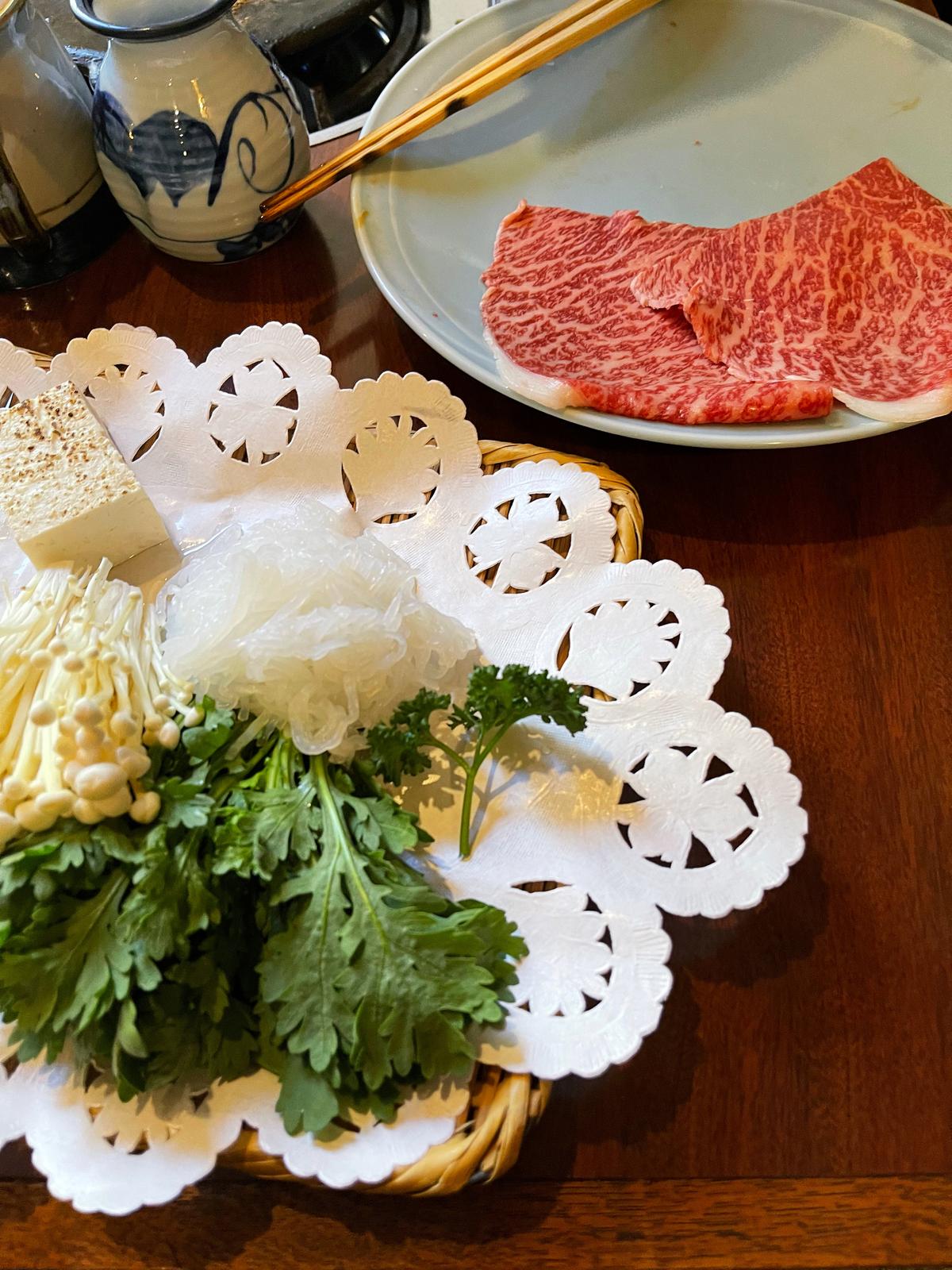 Platters of richly marbled slices of beef, chrysanthemum greens, noodles, mushrooms, and tofu are at the ready. (Melissa Uchiyama)