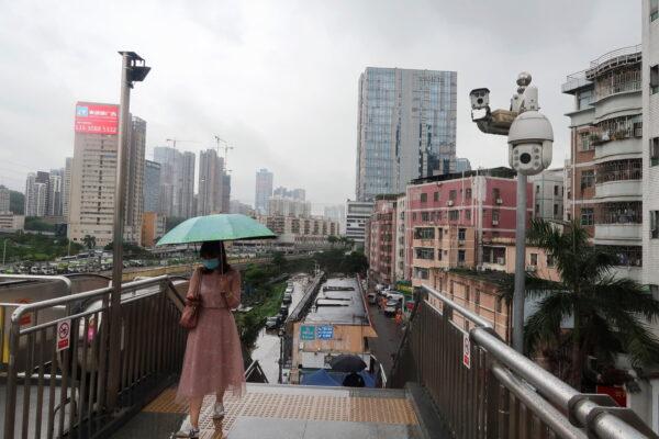 A woman holding an umbrella walks on a pedestrian bridge by surveillance cameras, near Caopu in Shenzhen's Luohu district, Guangdong Province, China, on July 5, 2022. (David Kirton/Reuters)