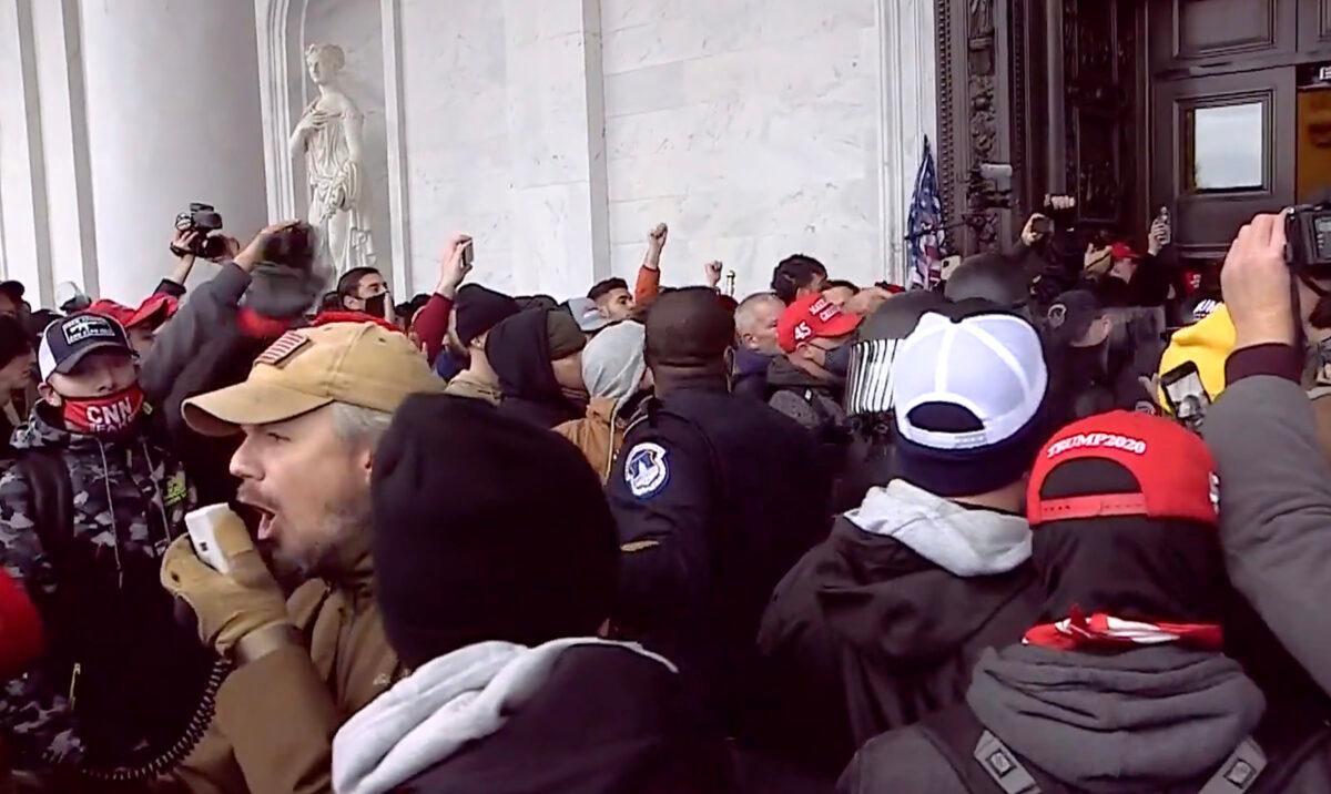 Retired police sergeant and Oath Keepers member Michael Nichols uses a bullhorn to make way for the police officers he was helping extract from the Capitol on Jan. 6, 2021. (U.S. DOJ/Screenshot via The Epoch Times)