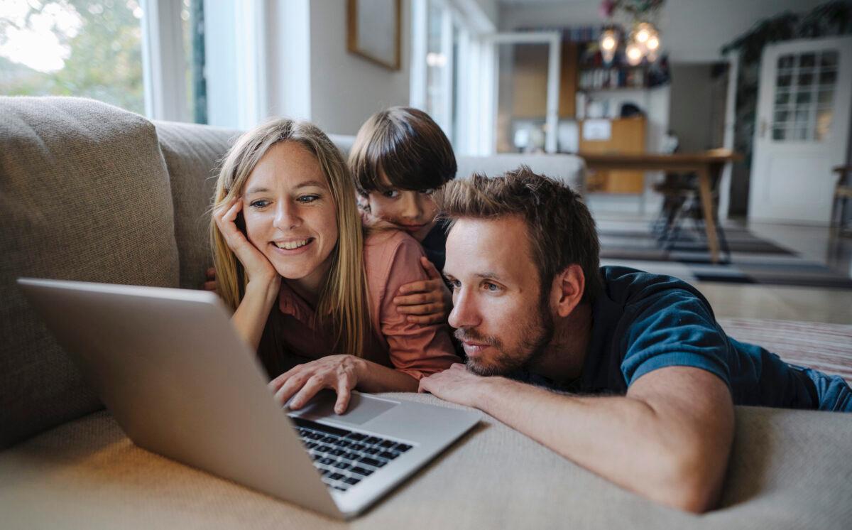 A family lying on a couch, using a laptop. (Westend61/Getty Images)