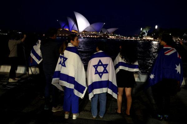 People with Israeli flags watch the Opera House while it is illuminated in blue to show solidarity with Israel in Sydney on October 9, 2023. (Photo by David GRAY / AFP) (Photo by DAVID GRAY/AFP via Getty Images)