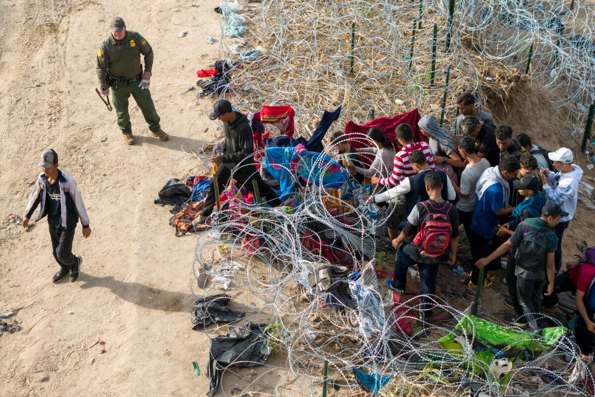 A U.S. Border Patrol agent supervises as immigrants walk into the United States after crossing the Rio Grande from Mexico, in Eagle Pass, Texas, on Sept. 30, 2023. The agent had cut coils of razor wire to let them pass through for processing. (John Moore/Getty Images)