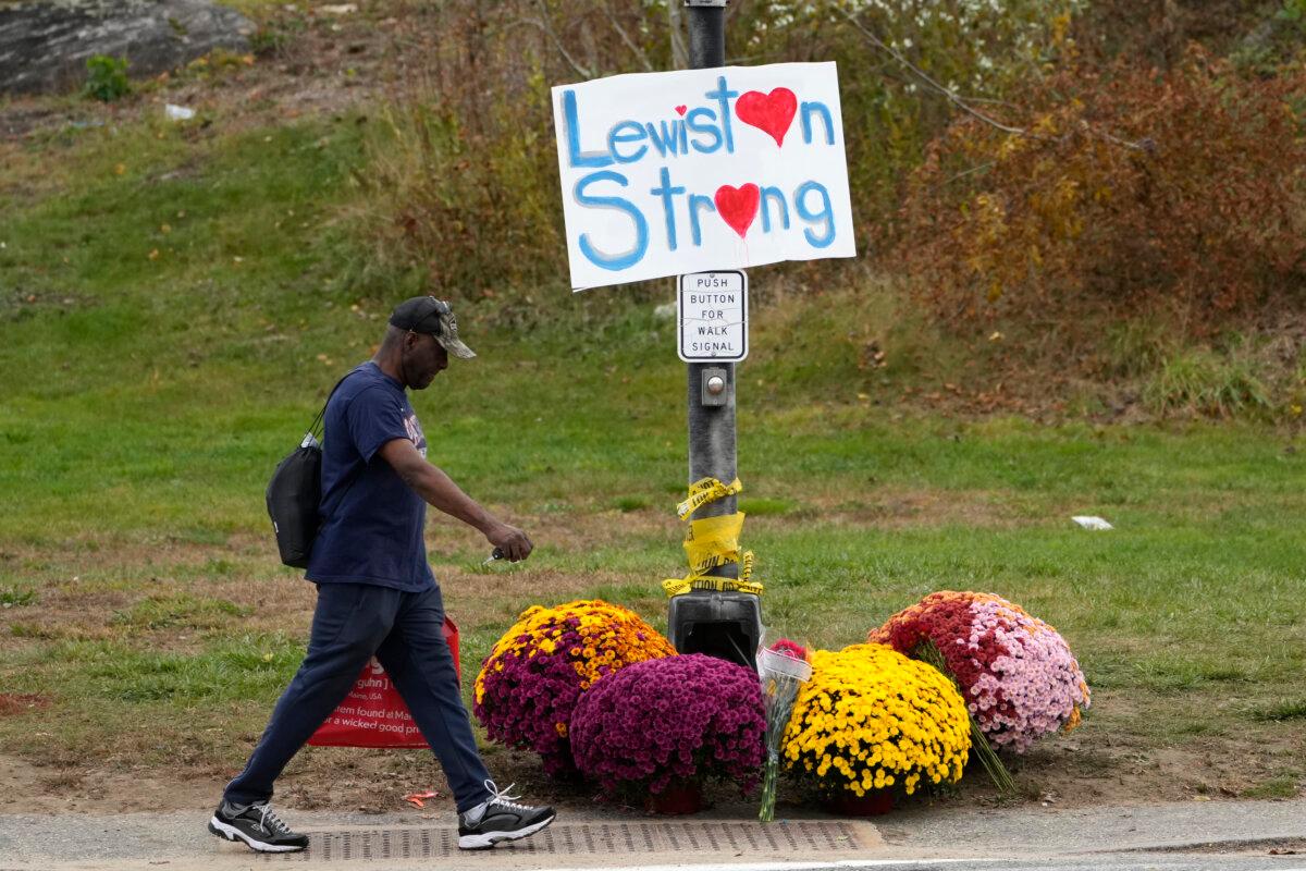 A man walks by flowers and a sign of support for the community in the wake of this week's mass shooting in Lewiston, Maine, on Oct. 28, 2023. (Robert F. Bukaty/AP Photo)