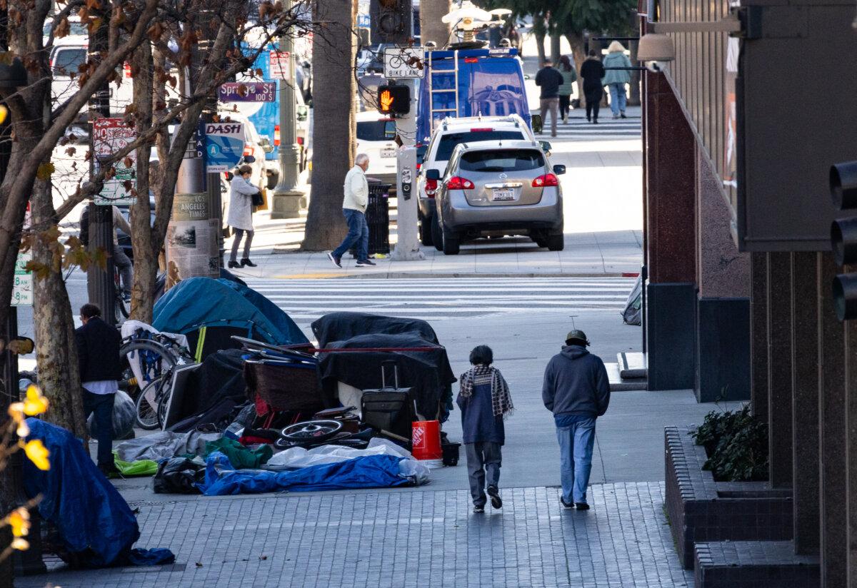 People pass homeless individuals in Los Angeles. Calif., on Jan. 11, 2024. (John Fredricks/The Epoch Times)