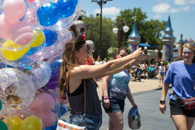 A woman takes a selfie with Disney balloons at the Magic Kingdom park in Orlando on May 22, 2016. (Benjamin Chasteen/Epoch Times)