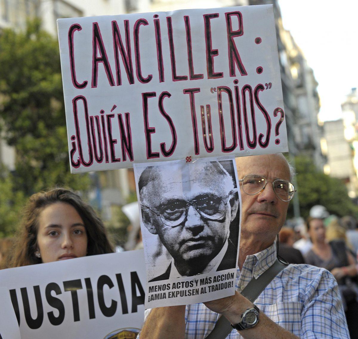 A man holds a placard with the picture of Argentinian Foreign Minister Hector Timerman and another one that reads "Foreign Minister: Who Is Your God" during a rally in front of the headquarters of the AMIA (Argentine Israelite Mutual Association), in Buenos Aires on January 21, 2015, to protest against the death of Argentine public prosecutor Alberto Nisman, who was found shot dead earlier, just days after accusing former President Cristina Fernández de Kirchner of obstructing a probe into a 1994 Jewish center bombing that killed 85 peiople and injured another 300. Nisman, 51, who was just hours away from testifying at a congressional hearing, was found dead overnight in his apartment in the trendy Puerto Madero neighbourhood of the capital. "I can confirm that a 22-caliber handgun was found beside the body," prosecutor Viviana Fein said. The nation's top security official said Nisman appears to have committed suicide. (Alejandro Pagni/AFP/Getty Images)