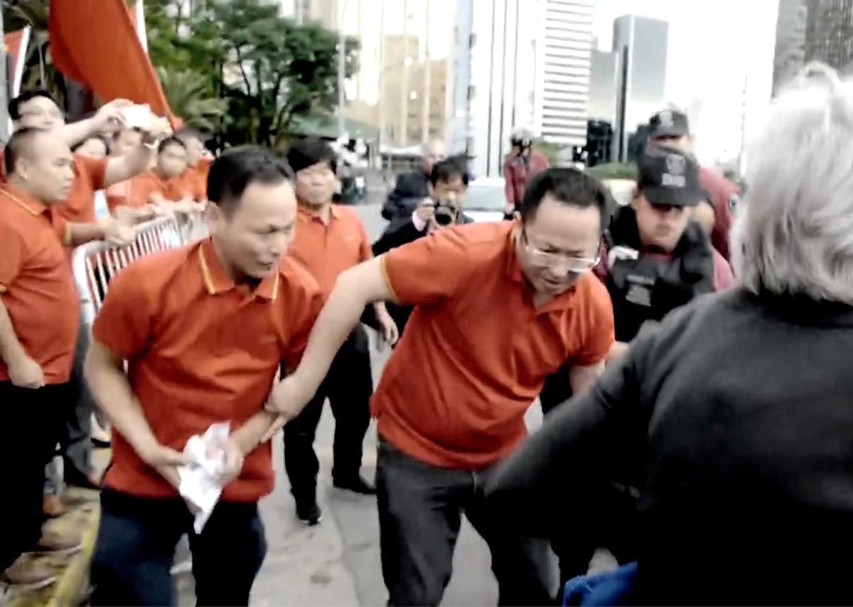 Chinese Communist Party supporters grab and scrunch up flyers from a Falun Gong practitioner's bag that had dropped to the ground on Nov. 29 in Buenos Aires, Argentina. (Screenshot/via YouTube)