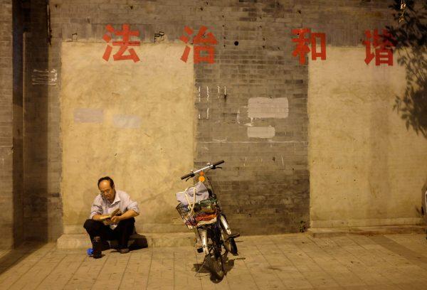 A resident sits near his bicycle while reading a book against a wall with the political slogans "Rule of Law and Harmony " in central Beijing on Aug. 18, 2014. (Jason Lee/Reuters)