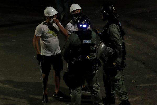 Men in white T-shirts and carrying poles talk to riot police in Yuen Long after attacking anti-extradition bill demonstrators at a train station in Hong Kong, on July 22, 2019. (REUTERS/Tyrone Siu)