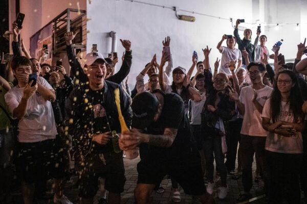 A pro-democracy supporter (C) opens a bottle of champagne outside a polling station to celebrate after pro-Beijing candidate Junius Ho lost a seat in the district council elections in Tuen Mun district of Hong Kong, early on Nov. 25, 2019. (Philip Fong/AFP via Getty Images)