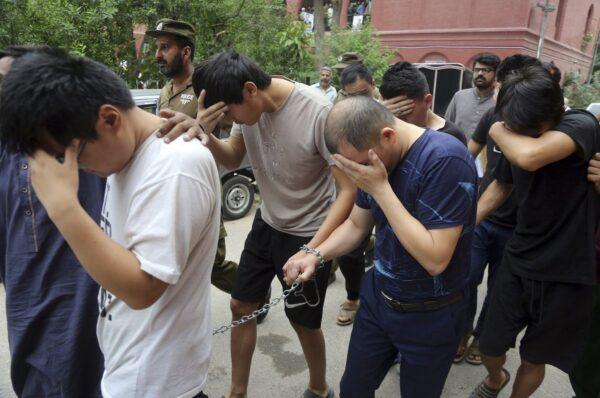 Detained Chinese nationals, accused of involvement in a trafficking gang to lure Pakistani women into fake marriages, try to shield their faces while they are escorted by Pakistan's Federal Investigation Agency officers to court in Lahore, Pakistan, on May 11, 2019. (K.M. Chaudary/AP Photo)