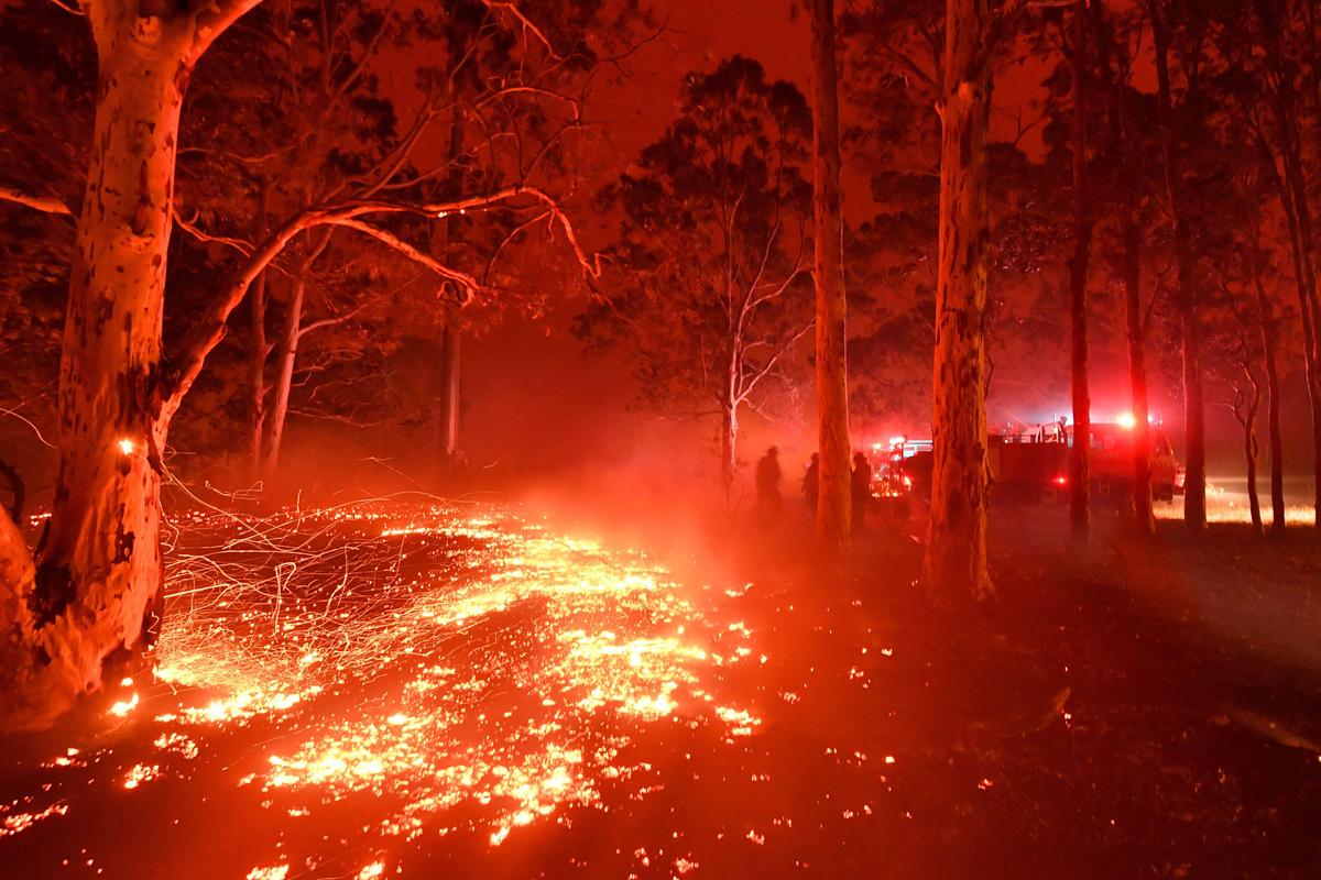 Burning embers cover the ground as firefighters (back R) battle against bushfires around the town of Nowra in the Australian state of New South Wales on Dec. 31, 2019. (©Getty Images | <a href="https://www.gettyimages.com/detail/news-photo/burning-embers-cover-the-ground-as-firefighters-battle-news-photo/1191093928?adppopup=true">SAEED KHAN</a>)