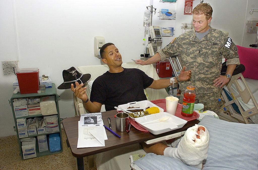 Gary Sinise listens to US Army CW 4 Leif Neely of Woodbridge, Virginia, tell about how he was wounded while flying his Kiowa Warrior helicopter on a mission over Mosul, Iraq, on May 20, 2007. (©Getty Images | <a href="https://www.gettyimages.com/detail/news-photo/in-this-handout-provided-by-the-uso-actor-gary-sinise-news-photo/74210354?adppopup=true">Mike Theiler/USO</a>)