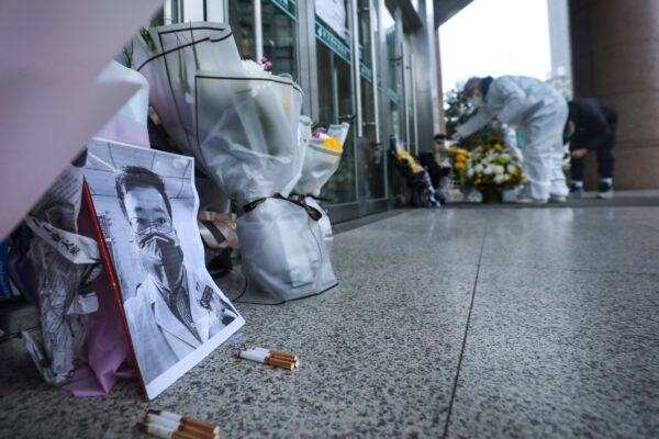 People pay condolence in front of flowers lying near a photo of the late Dr. Li Wenliang at a hospital in Wuhan in central China's Hubei Province, on Feb. 7, 2020. Li was reprimanded for warning about China's new virus. His death triggered an outpouring of praise and fury that communist authorities put politics above public safety. (Chinatopix via AP)
