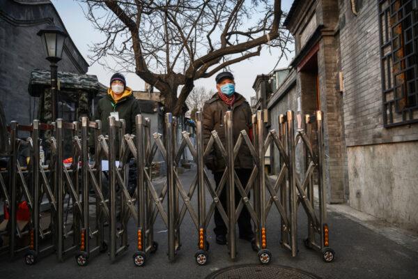 A Chinese woman takes delivery of wine from a man as they both wear protective masks at a barricade placed a local neighborhood committee to control people entering and exiting a local hutong as part of government efforts to control the spread of the coronavirus in Beijing on Feb. 19, 2020. (Kevin Frayer/Getty Images)