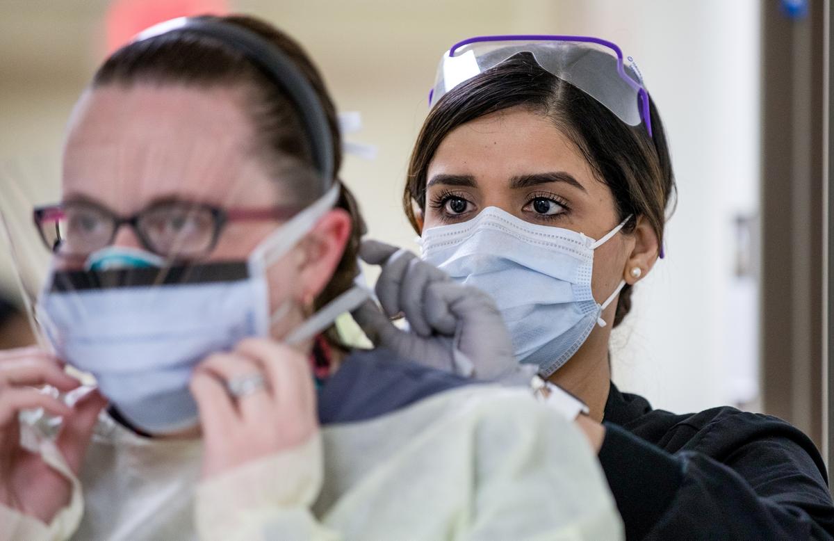 Melissa Sweeney, LPN, helps Renee Grimm don her personal protective equipment before dealing with a patient at Madigan Army Medical Center's enhanced CCP virus screening site Winder Clinic on Joint Base Lewis-McChord in Tacoma, Washington, on March 24, 2020. (John Wayne Liston/U.S. Army/Handout via Reuters)