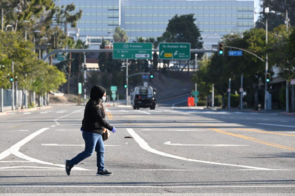 A woman wears a mask as she crosses an empty street near the Los Angeles Convention Center in downtown Los Angeles, California, on March 30, 2020. (Robyn Beck/AFP via Getty Images)