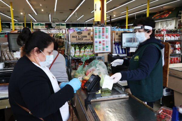 A shopper and cashier both wear masks and gloves and the cashier also has on a plastic visor at the checkout station at Pat's Farms grocery store in Merrick, New York, on March 31, 2020. (Al Bello/Getty Images)