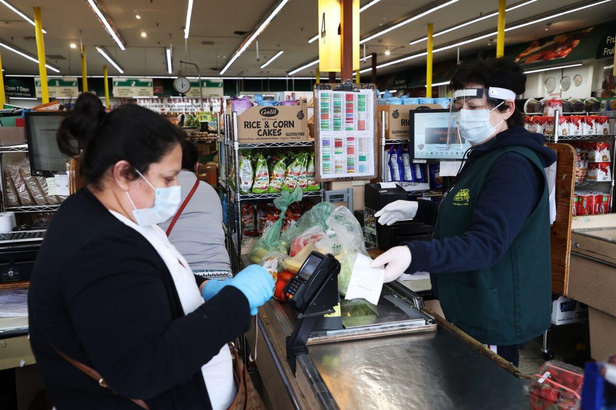 A shopper and cashier both wear masks and gloves at the checkout station Pat's Farms grocery store in Merrick, New York, on March 31, 2020. (Al Bello/Getty Images)