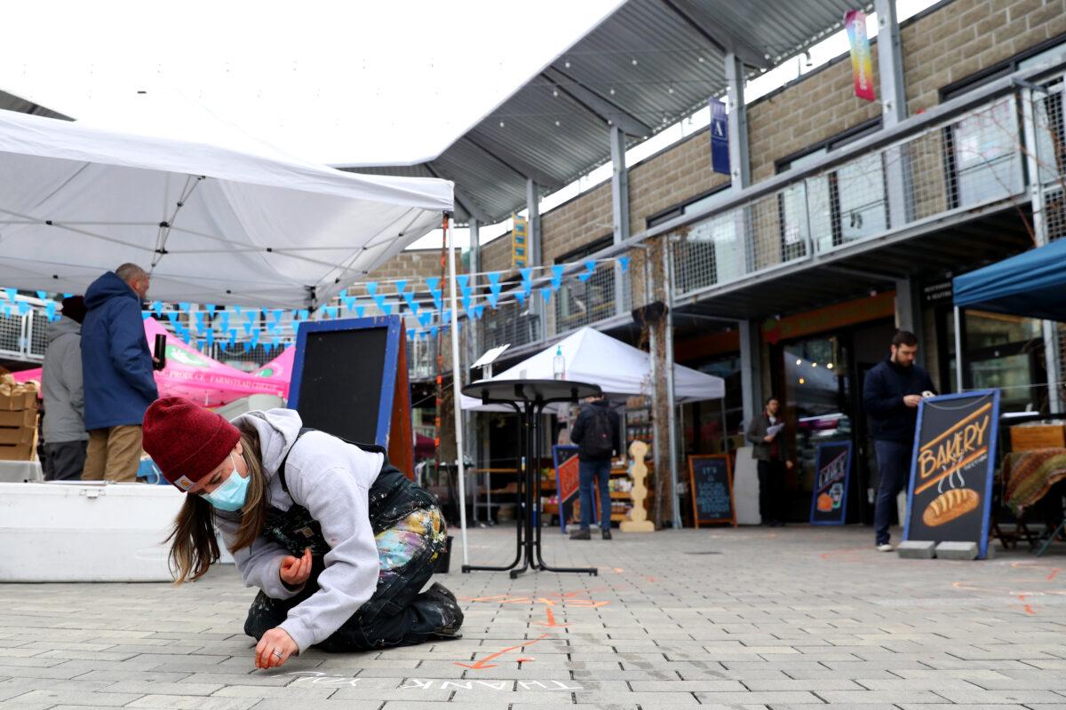 To encourage social distancing, a volunteer marks the walkway at an outdoor grocery store at Bow Market in Somerville, Mass., on March 21, 2020. (Maddie Meyer/Getty Images)