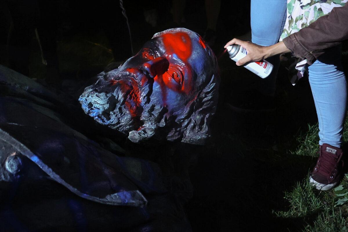 A vandal sprays paint on the toppled statue of Albert Pike in Washington on June 19, 2020. (Jonathan Ernst/Reuters)