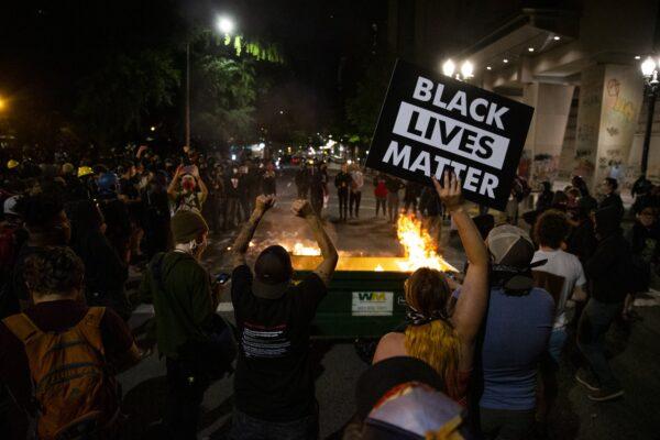 A waste receptacle that had been moved into the intersection of SW 3rd Avenue and Main Street in Portland is set on fire as protesters gathered downtown on July 10, 2020. (Dave Killen/The Oregonian via AP)