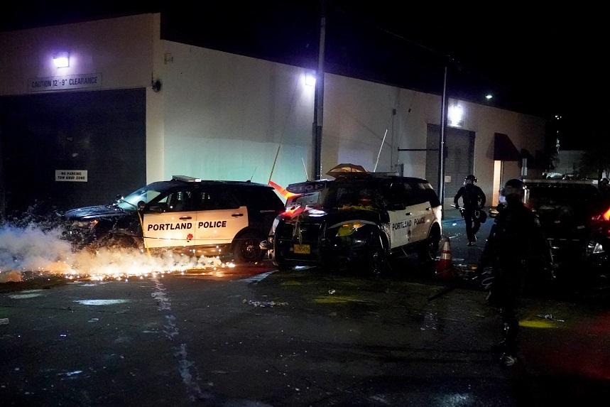A smoke grenade ignites beneath a vandalized police cruiser at the Portland Police Bureau North Precinct during a protest 2020 in Portland, Ore., on Aug. 22. (Nathan Howard/Getty Images)