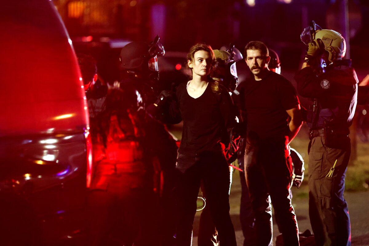 A woman and a man are detained by police officers during rioting in Portland, Ore., on Sept. 5, 2020. (Carlos Barria/Reuters)