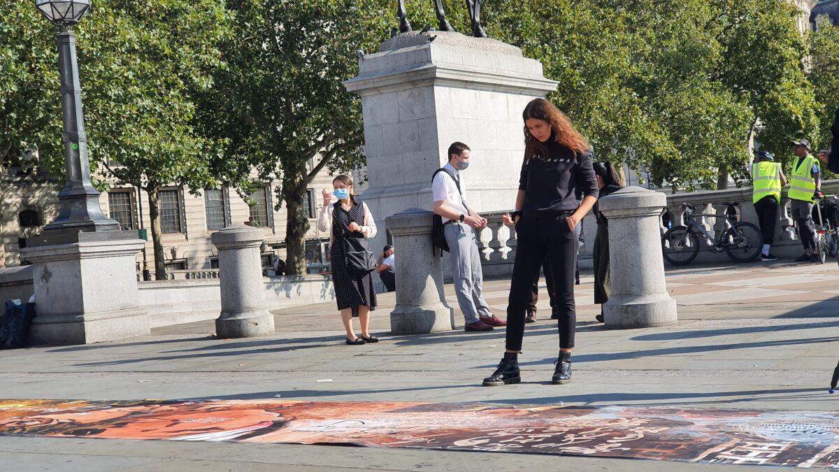 A women looks at a 10-meter painting about Hong Kong's pro-democracy movement, by Otto Yuen, known as the Lennon Wall painter, in Trafalgar Square, London, on Sept. 21, 2020. (Lily Zhou/The Epoch Times)