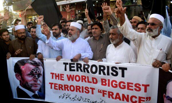 Pakistan traders hold a banner with a defaced picture of French President Emmanuel Macron during a protest against the publishing of caricatures of the Prophet Muhammad, in Peshawar, Pakistan, on Oct. 26, 2020. (Muhammad Sajjad/AP Photo)