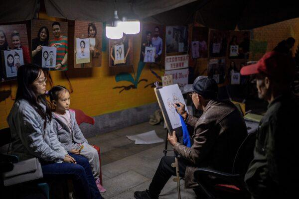 A woman and a girl posing for a portrait at an artist stall on a street in the 798 art district in Beijing, China on Oct. 18, 2020. (NICOLAS ASFOURI/AFP via Getty Images)