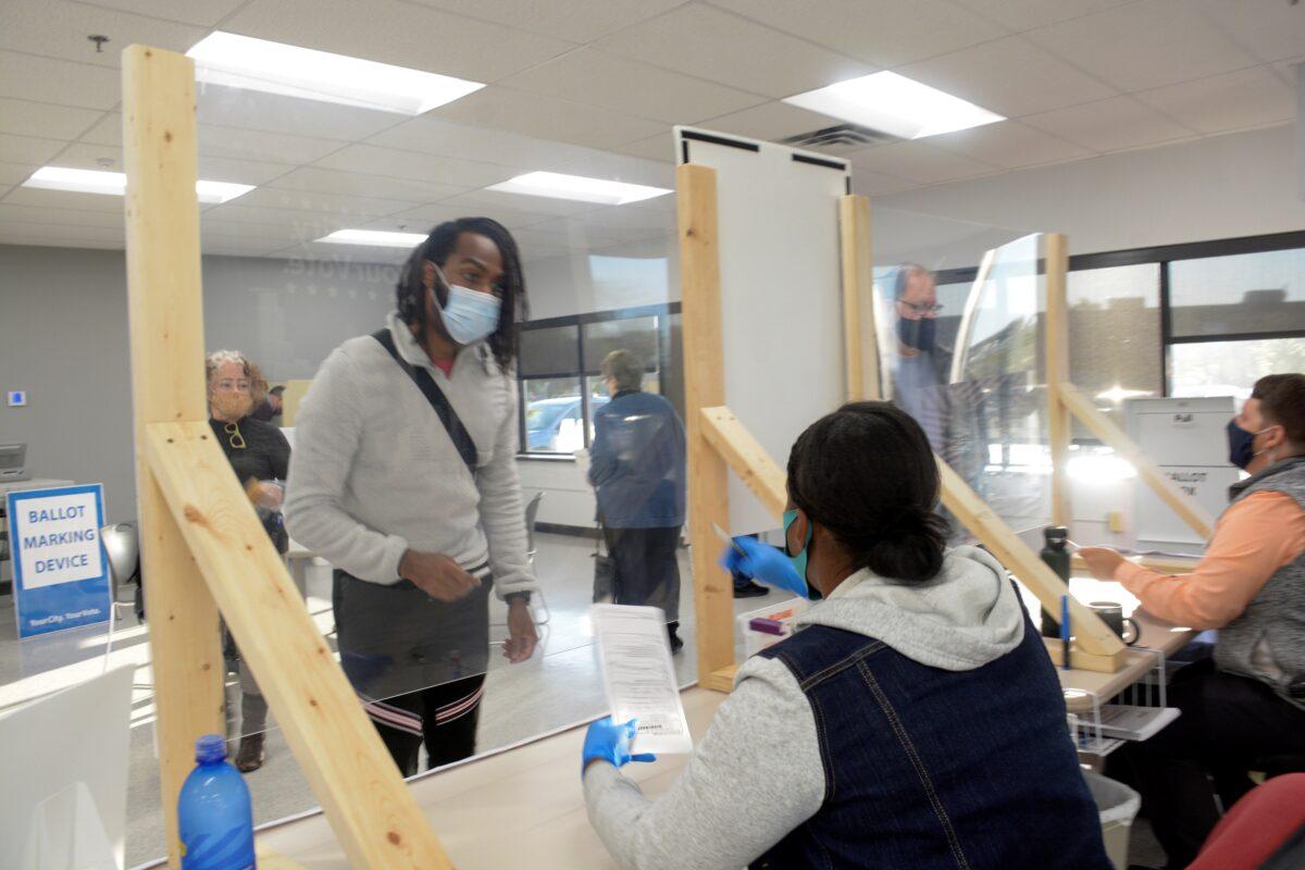 A voter talks to poll workers as he receives his ballot during early voting in Minneapolis, Minn., on Sept. 18, 2020. (Julio Cesar Chavez/Reuters)