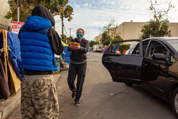 A woman hands items to a homeless person in the Venice neighborhood of Los Angeles on Jan. 27, 2021. (John Fredricks/The Epoch Times)