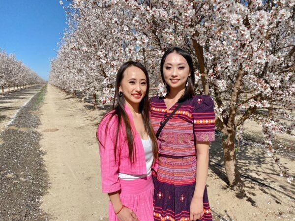 Xee Xiong (L) and her sister Shoua Xiong (R) pose in Hmong ethnic outfits next to the blossoms in Fresno, Calif., on Feb. 27, 2021. (Ilene Eng/The Epoch Times)