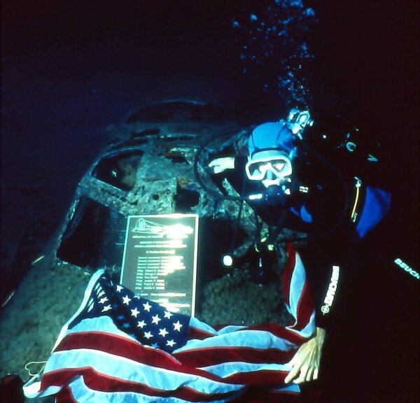 Marine biologist John Christopher Fine poses with the American flag and a plaque on a B-17 bomber underwater off the coast of Calvi, Corsica. (Courtesy of John Christopher Fine)