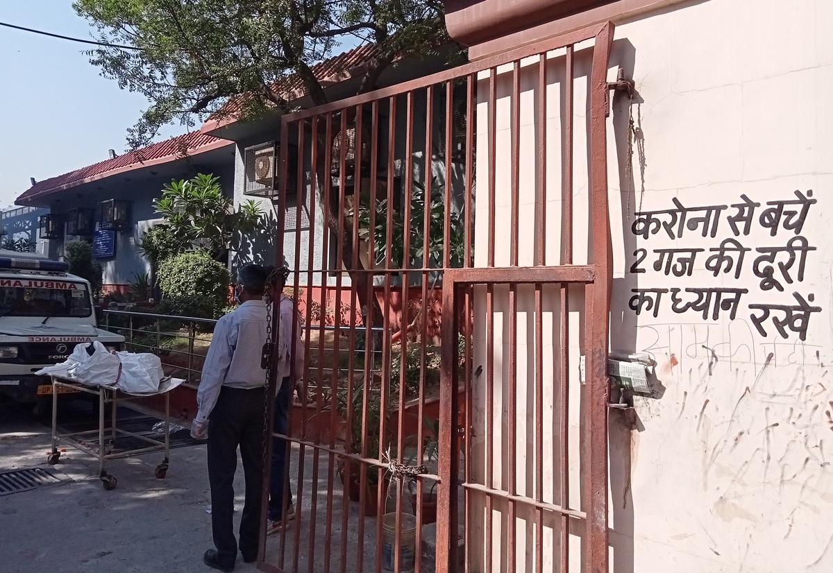 A corpse lies on a stretcher at the entrance of the Nigam Bodh Ghat, while the notice on the wall displays an appeal in Hindi for cautionary social distancing, in New Delhi on April 24, 2021. (Venus Upadhayaya/Epoch Times)
