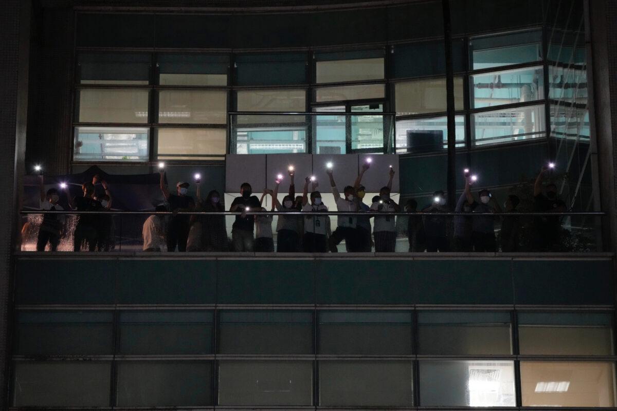 Staff members wave flashlights to their supporters at the Apple Daily headquarters in Hong Kong, on June 23, 2021. (AP Photo/Kin Cheung)