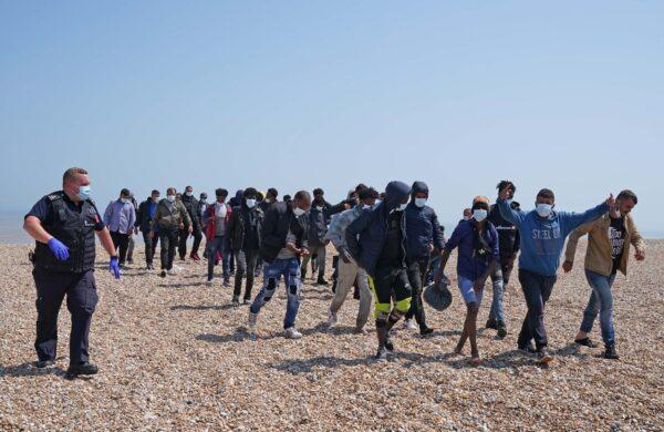 A group of people thought to be migrants are escorted by Border Force officers following a small boat incident in the Channel, from the beach in Dungeness, Kent, England, on July 20, 2021. (Gareth Fuller/PA)