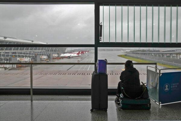 A passenger sits on her luggage watching the passenger airplanes parked on the tarmac after all flights were canceled at Pudong International Airport in Shanghai, on July 25, 2021. (Andy Wong/AP Photo)