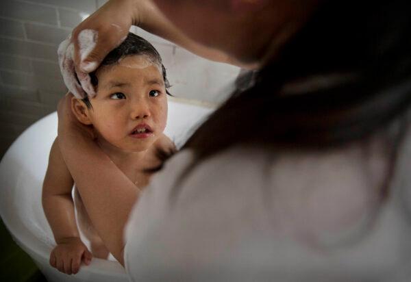 An orphaned girl is bathed by a worker at a foster care center on April 2, 2014 in Beijing, China. China's orphanages and foster homes used to be filled with healthy girls, reflecting the country's one-child policy and its preference for sons. Now the vast majority of orphans are sick or disabled. China says it has 576,000 orphans in its child welfare system, but outside groups put the number at closer to a million. The parents who abandon them either cannot afford treatment or feel unable to cope with raising a child with special needs. (Photo by Kevin Frayer/Getty Images)