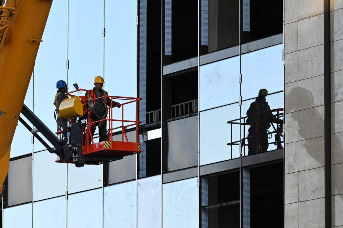 Workers prepare to install a window panel at a construction site in Beijing on Oct. 19, 2021. (Greg Baker/AFP via Getty Images)