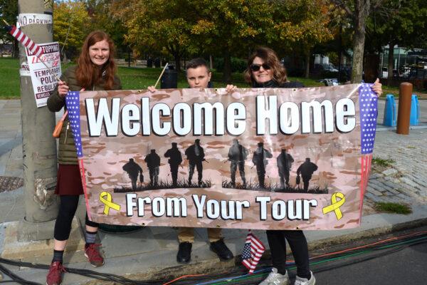 Christina Whitney(right), an Iraq War veteran’s wife, holds a banner of “Welcome Home From Your Tour” with her daughter and son to greet the parade during the 7th Annual Veterans Parade & Festival in Philadelphia, Pa., on Nov. 7, 2021. (Frank Liang/The Epoch Times)