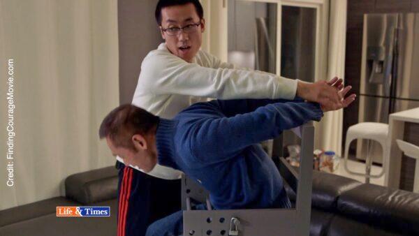 In the award-winning documentary “Finding Courage,” Leo Wang (L) and his son Martin demonstrate Leo's torture when he was jailed in China for printing flyers. Wang spent 12 years in prison for making flyers that exposed the persecution of Falun Gong. The chair he is sitting in is a replica he built himself. (Swoop Films/Paulio Shakespeare/Screenshot via The Epoch Times)